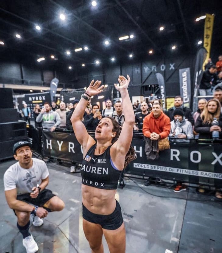 Lauren Weeks throwing a wall ball during a Hyrox competition, crowd behind her
