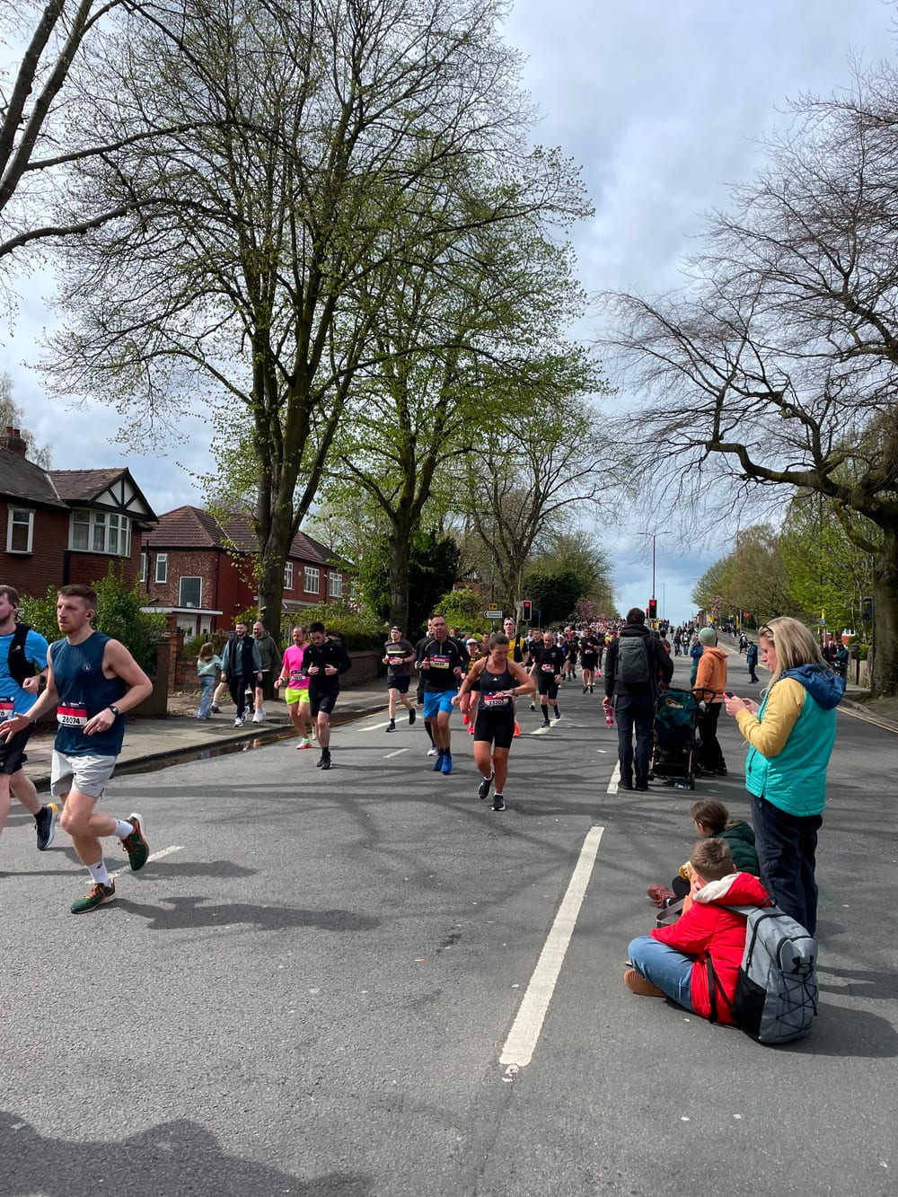 Runners and spectators on a tree-lined Manchester street