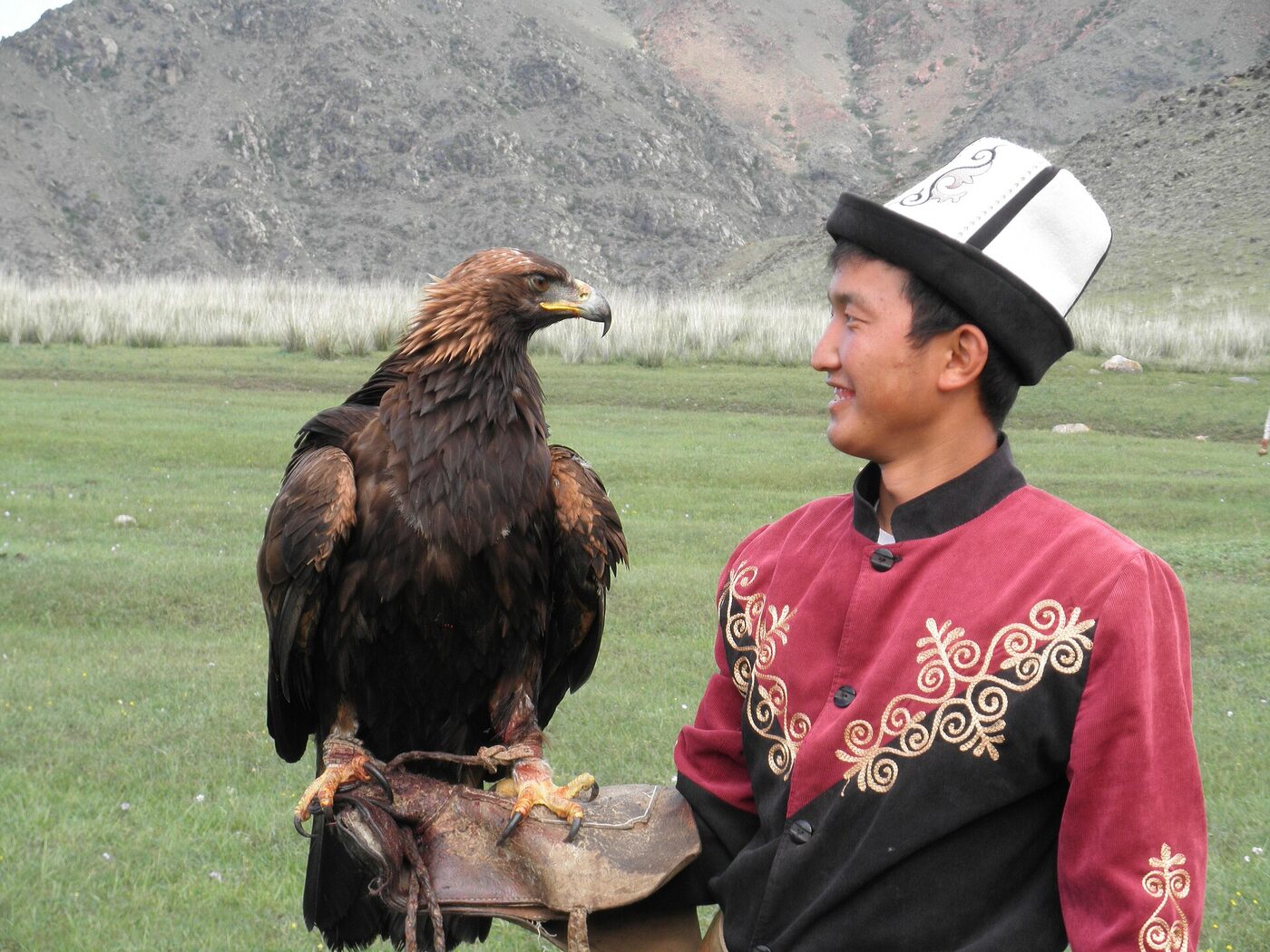 A Kyrgyz eagle hunter in a red embroidered coat with a golden eagle perched on his gloved hand